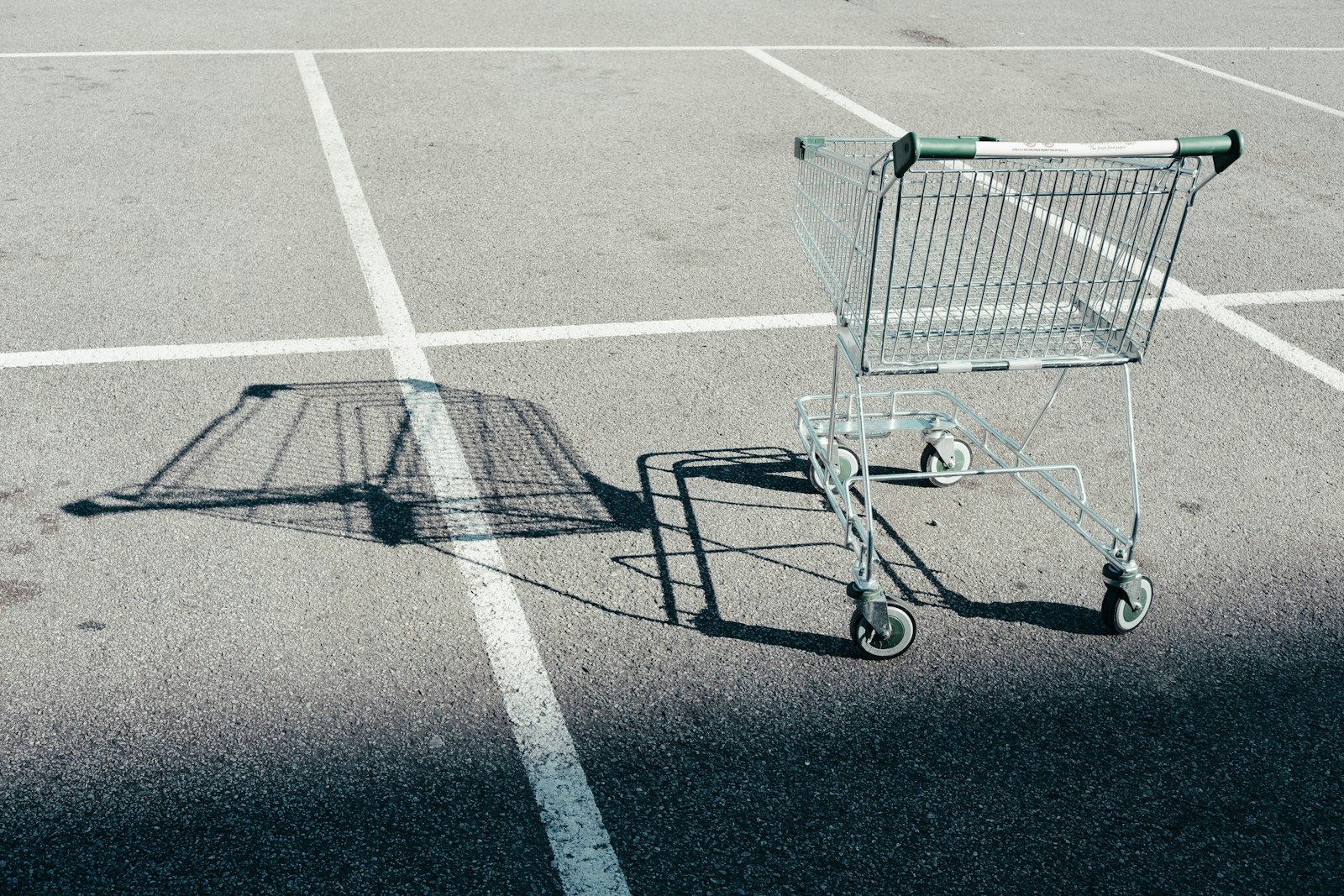 Ein einzelner leerer Einkaufswagen steht auf einem leeren Parkplatz und wirft einen langen Schatten über die markierten Stellplätze