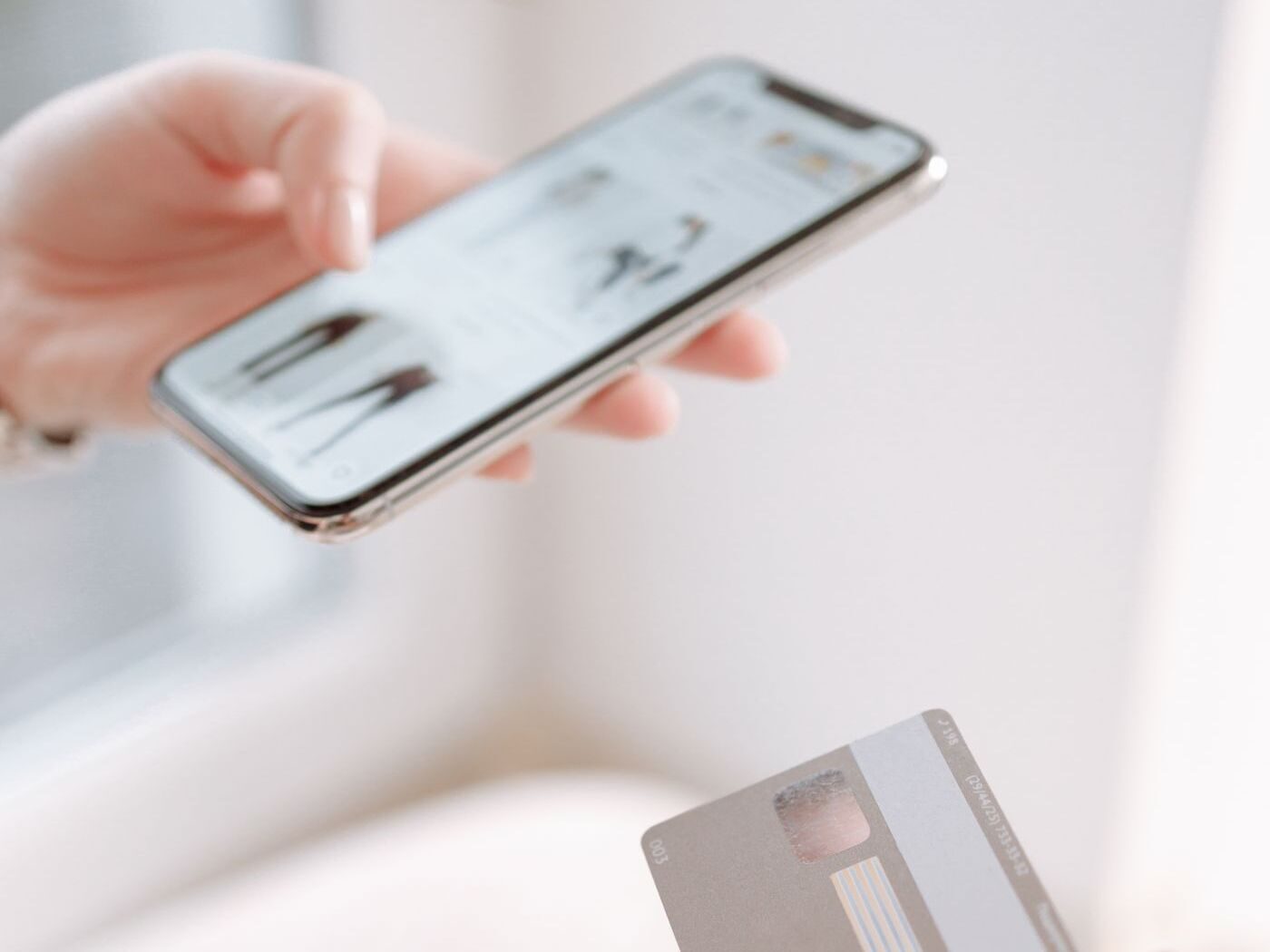 A hand holding a phone open to a store, a bank card resting in the other hand, ready to pay